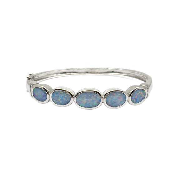 A sterling silver bangle featuring a line of oval-shaped Australian doublet opals, each set in a secure bezel setting, interspersed with small, round cubic zirconia for a delicate sparkle. The bracelet's design allows for the natural beauty of the opals to shine, making it a versatile piece for various occasions. | Fremantle Opals